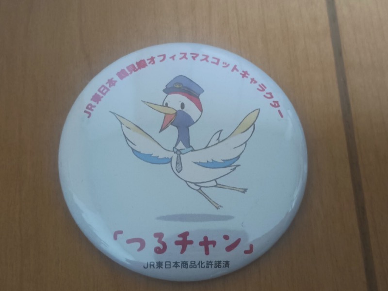 缶バッジ。駅員の帽子とネクタイをつけた鶴が羽を広げている。つるチャンの文字